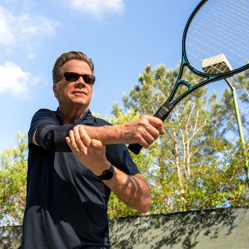 Person wearing the OrthoSleeve Elbow Bracing Sleeve in Black while playing tennis