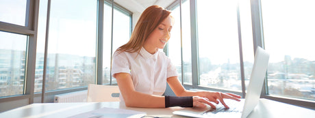 Woman working on a laptop wearing a wrist compression sleeve