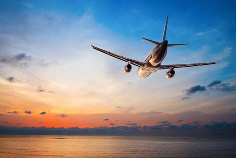 An airplane flying over water through a beautiful sunset