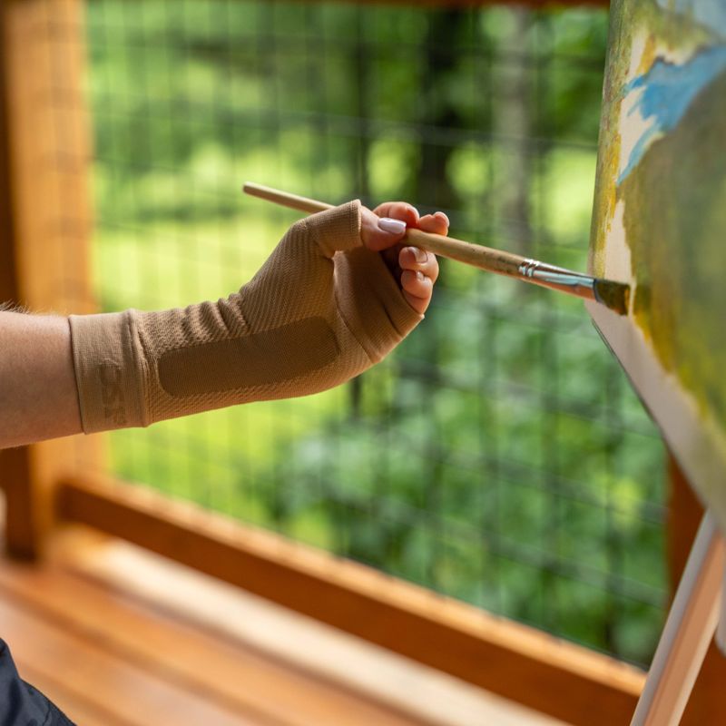 Woman wearing the tan OrthoSleeve Compression Wrist Sleeve while painting a picture