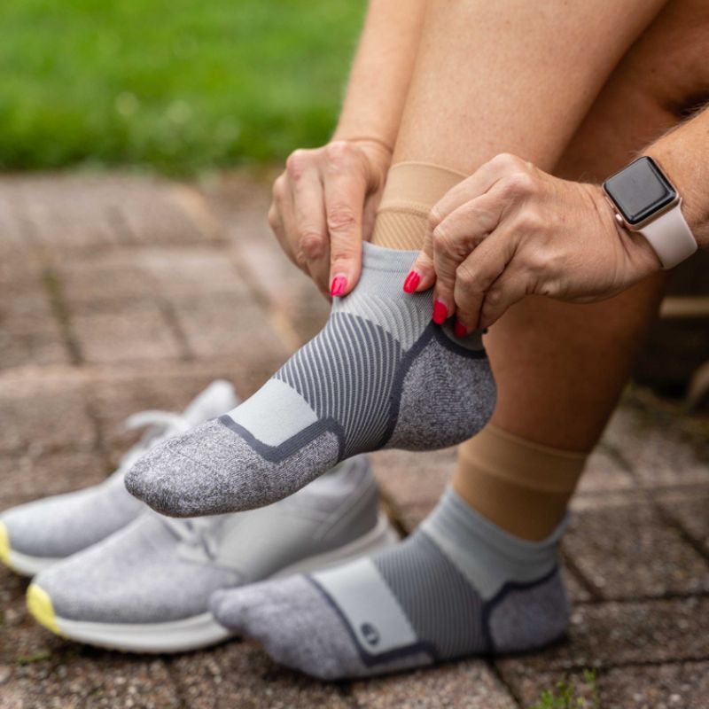 Woman putting on a pair of grey no show OrthoSleeve Wellness Care Socks