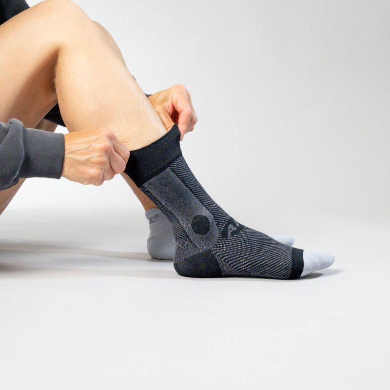 Person putting on black ankle sleeve on a white background