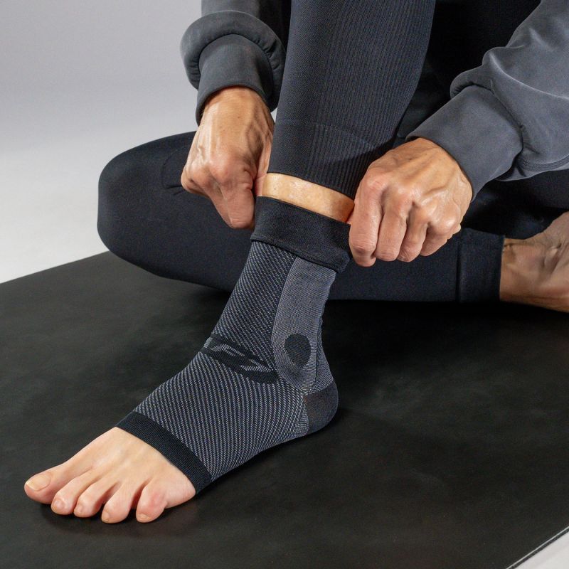 Person wearing a black ankle sleeve on a black workout mat.