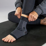 Person wearing a black ankle sleeve on a black workout mat.
