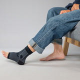 Person wearing black ankle sleeve with rolled-up jeans on a gray background