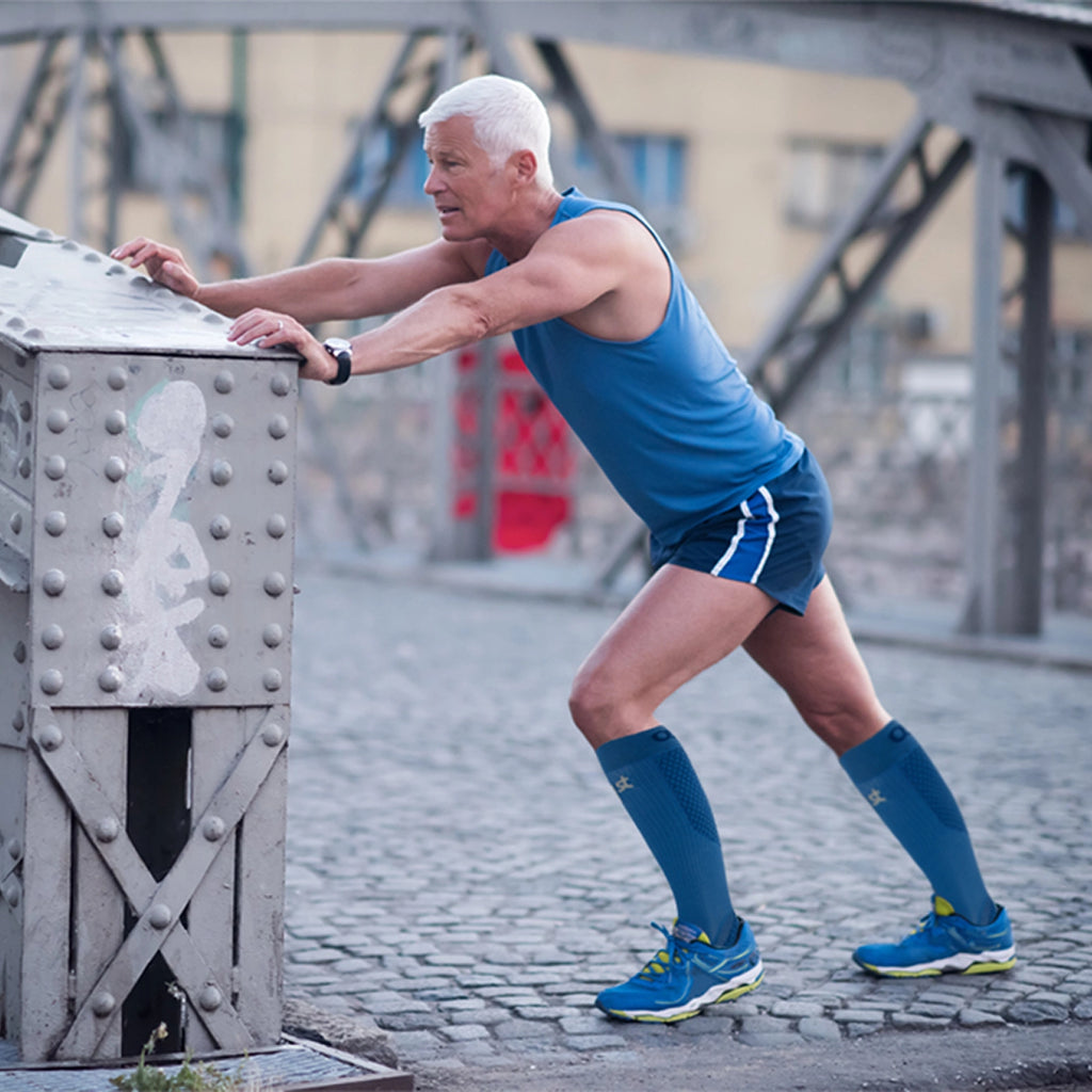 A man stretching outside before a run while wearing the blue compression bracing socks
