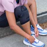 Close up of a woman lacing her shoes before exercising outside while wearing the compression knee brace