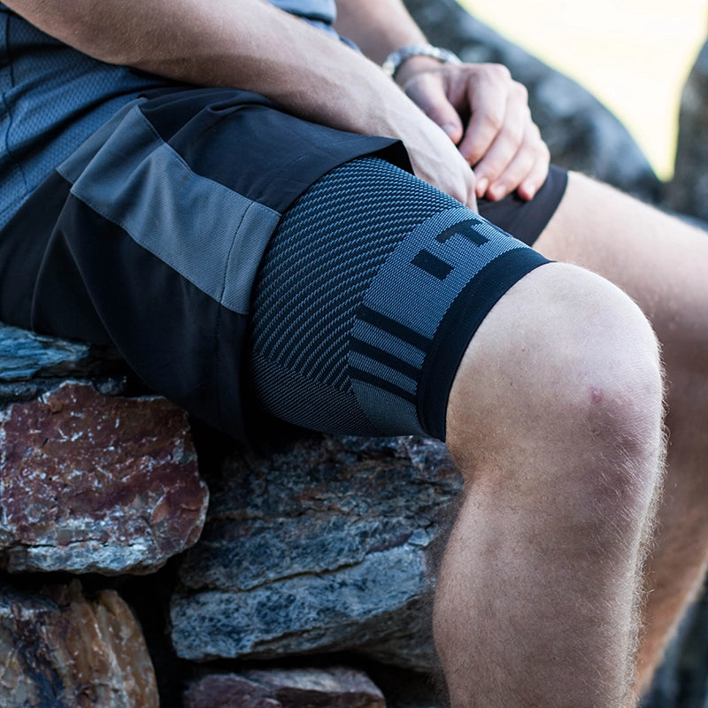 A man sitting on a stone wall in workout clothes wearing the Orthosleeve thigh compression sleeve