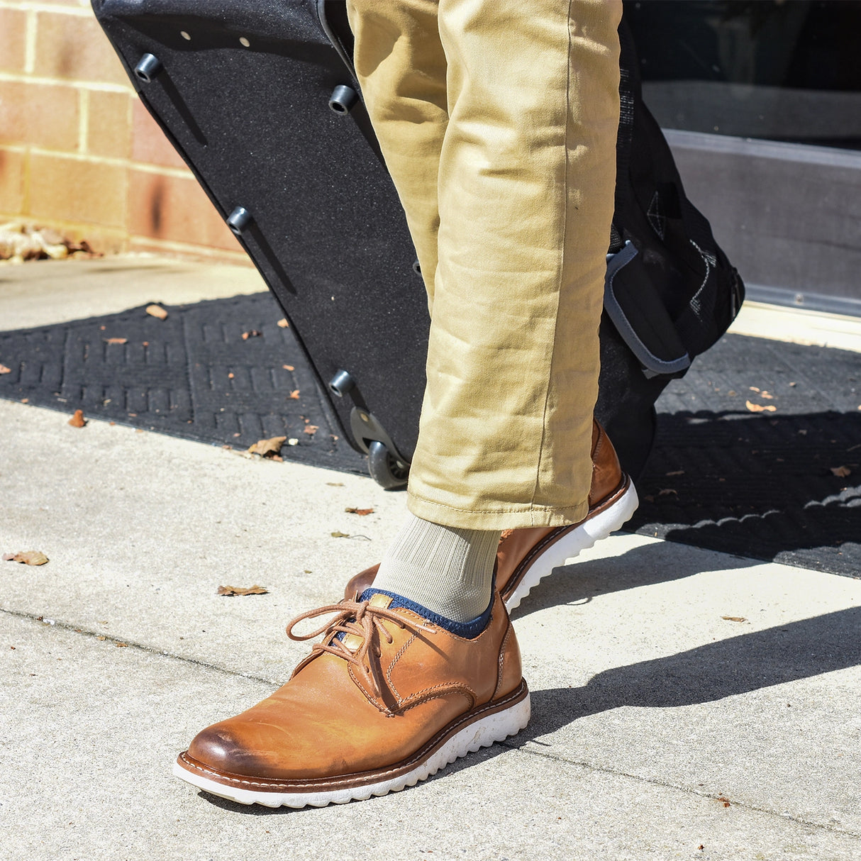 Close up of a man wearing tan, medical grade compression socks in tan leather work shoes carrying a bag for travel out of the building