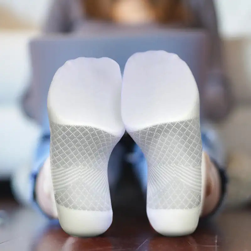 Close up image of a woman's feet up on a table while she's working on her laptop wearing white Plantar Fasciitis Socks